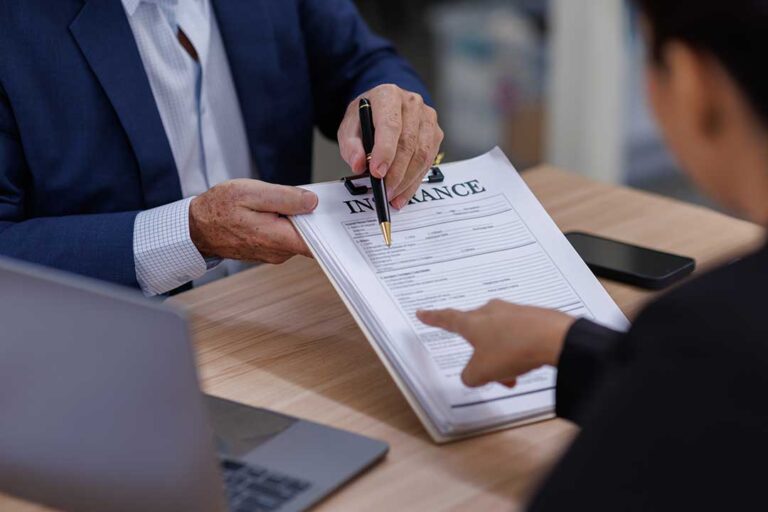 A person reviewing auto insurance documents and calculator at a kitchen table with a car key nearby.
